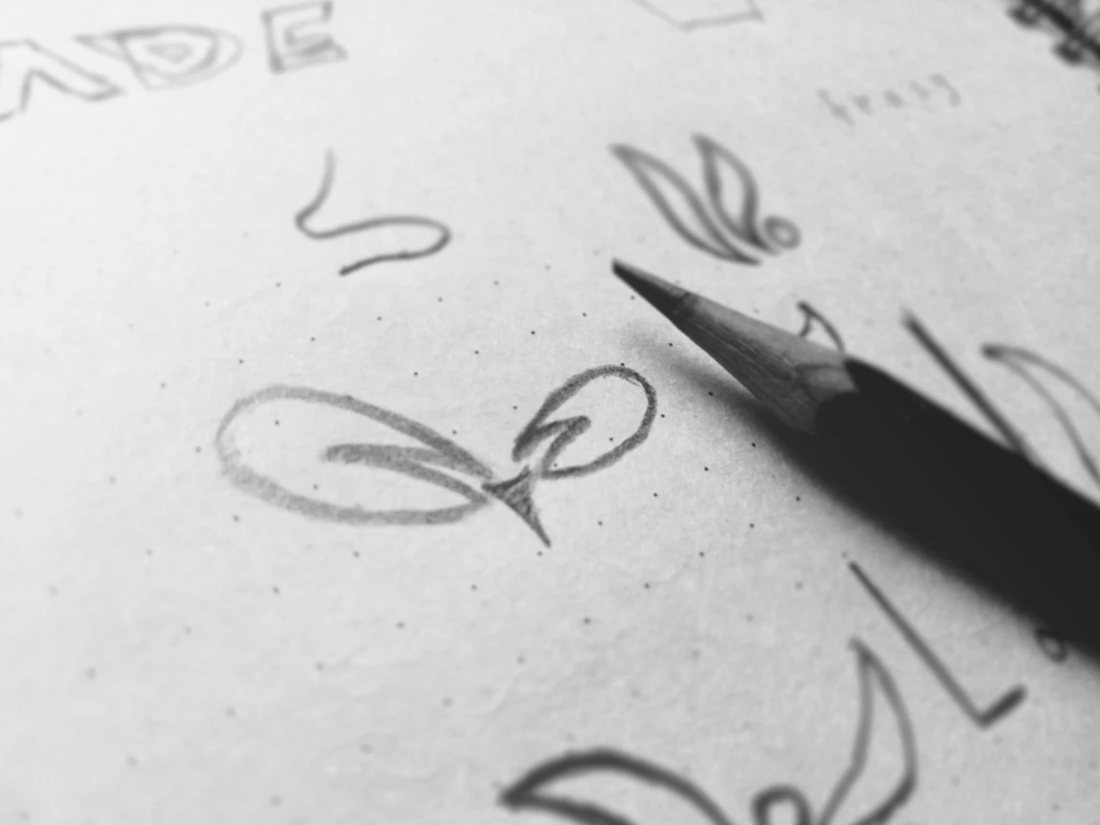 Logo concepts sketched in pencil on dotted paper, pencil still in hand